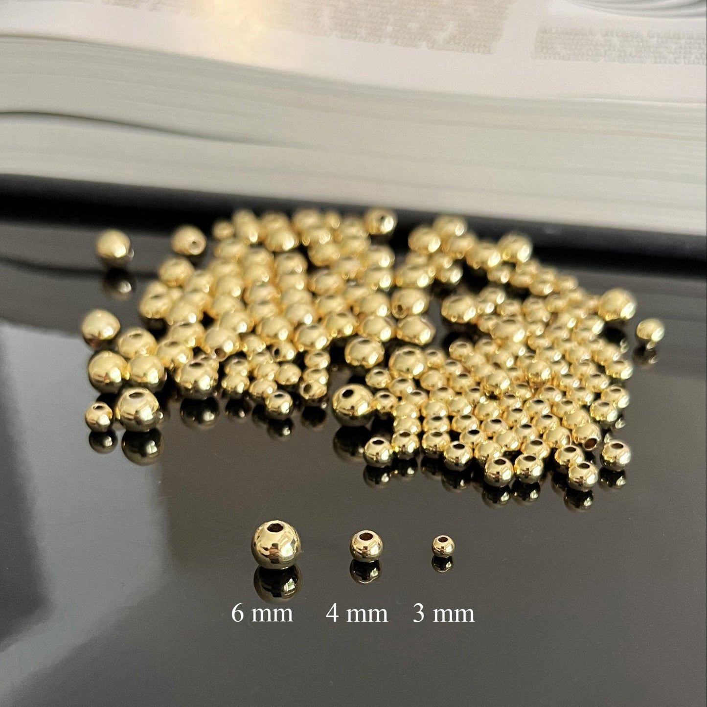 Gold beads of different sizes on a reflective surface with measurement labels.