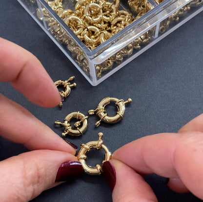 Gold jewelry components being handled with a clear container of more components in the background.