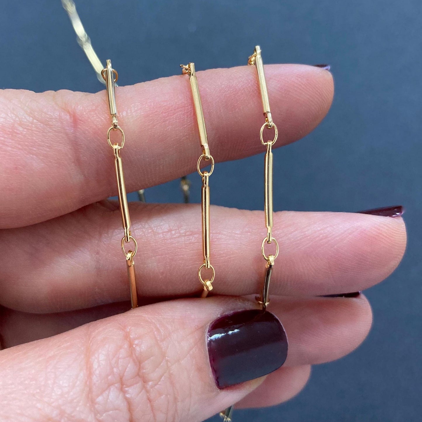 Gold chain earrings held between fingers against a dark background