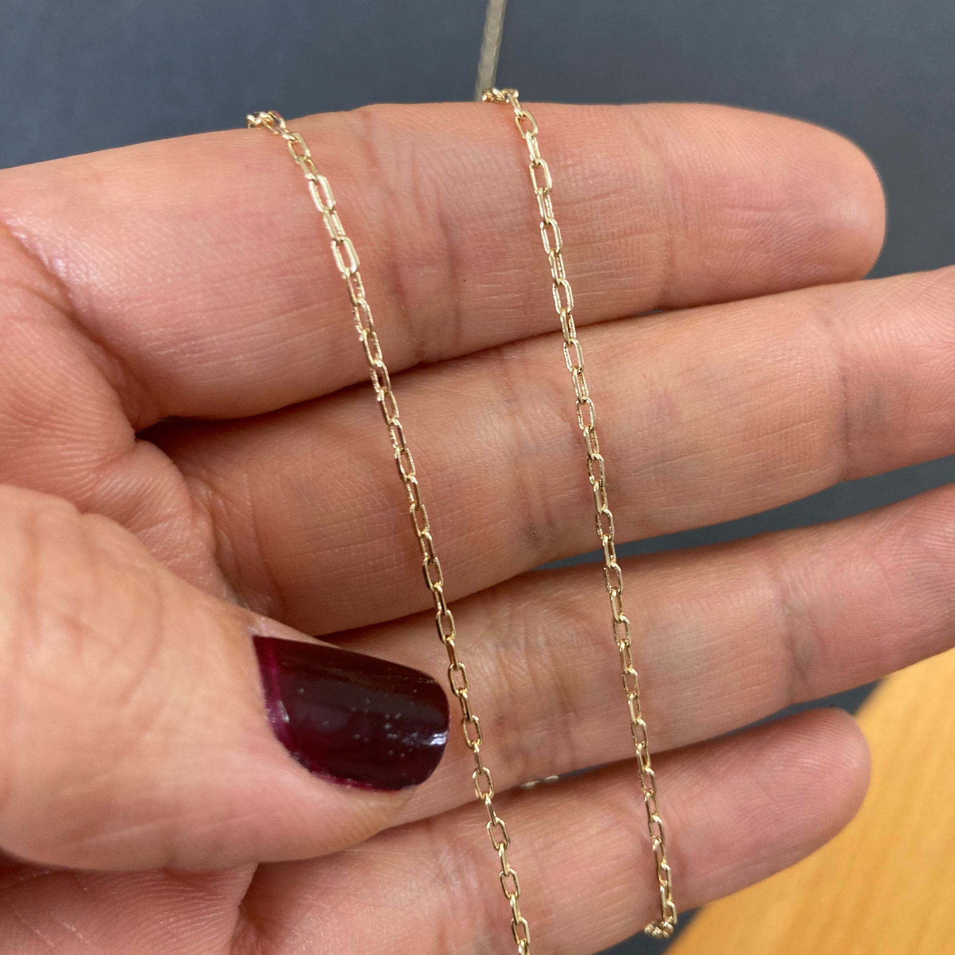 Gold chain held between fingers against a neutral background