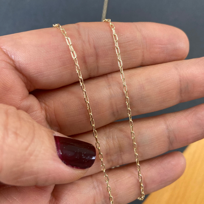 Gold chain held between fingers against a neutral background