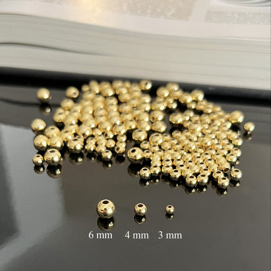 Gold beads of different sizes on a reflective surface with measurement labels.