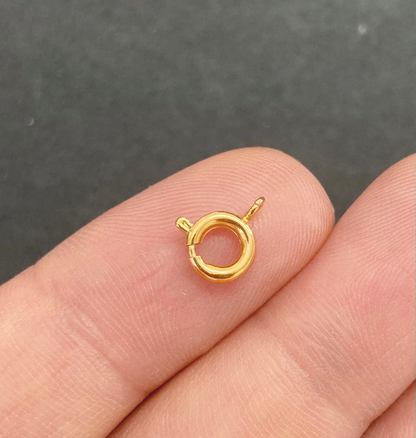 Gold jewelry clasp held between fingers on a dark background